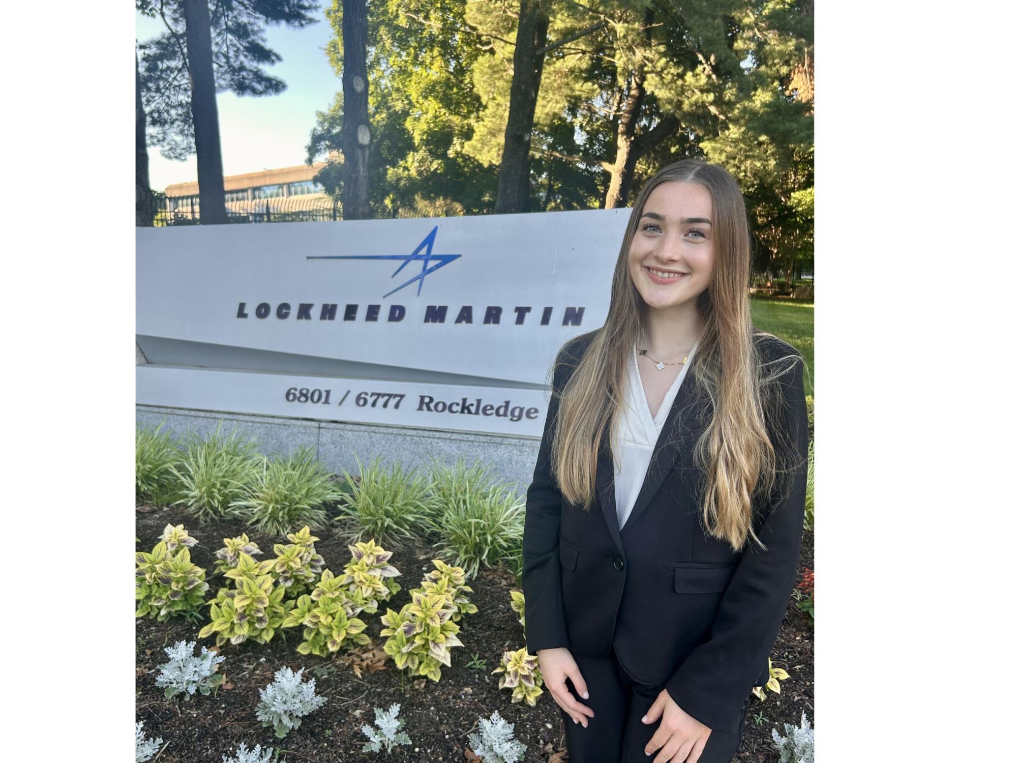 Person with long brown hair poses next to Lockheed Martin sign