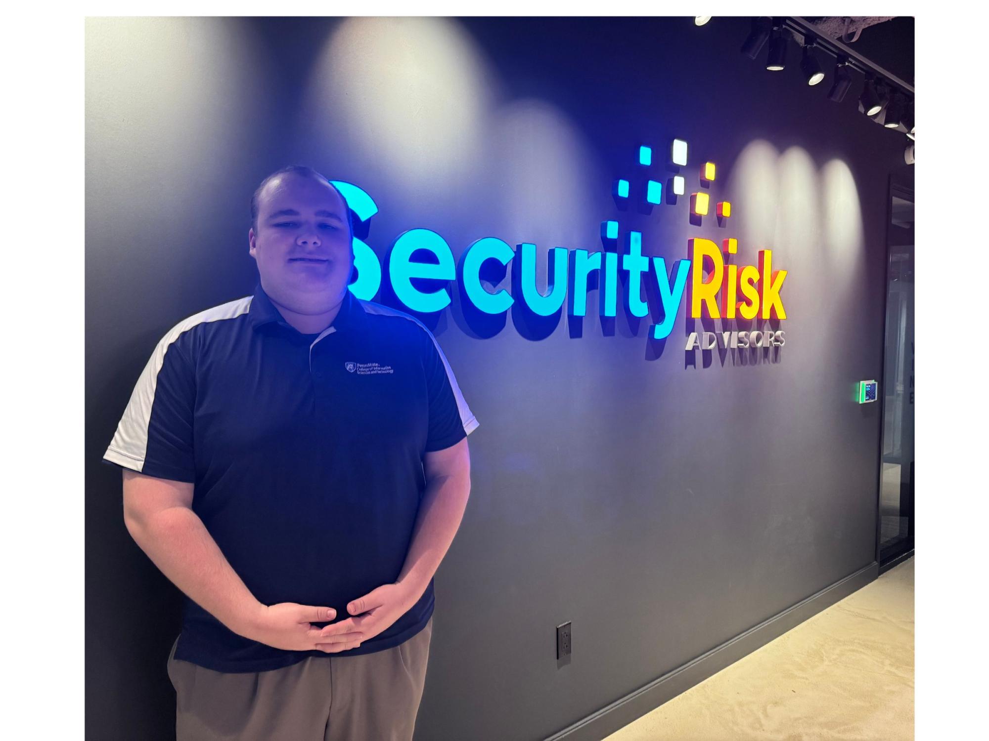 Person in blue and white golf shirt poses next to Security Risk Advisors signage