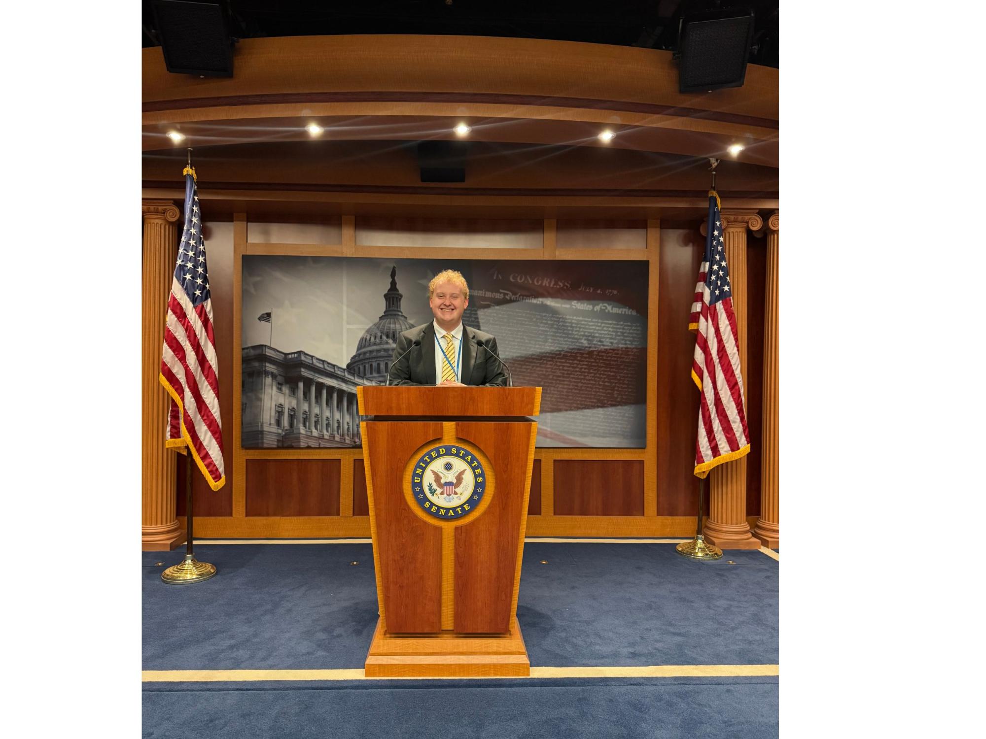 College student smiles from podium in the Senate chamber of the U.S. Capitol