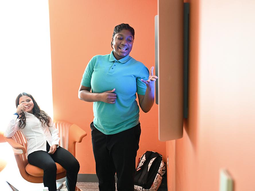 A high school student in a teal shirt gives a research presentation.