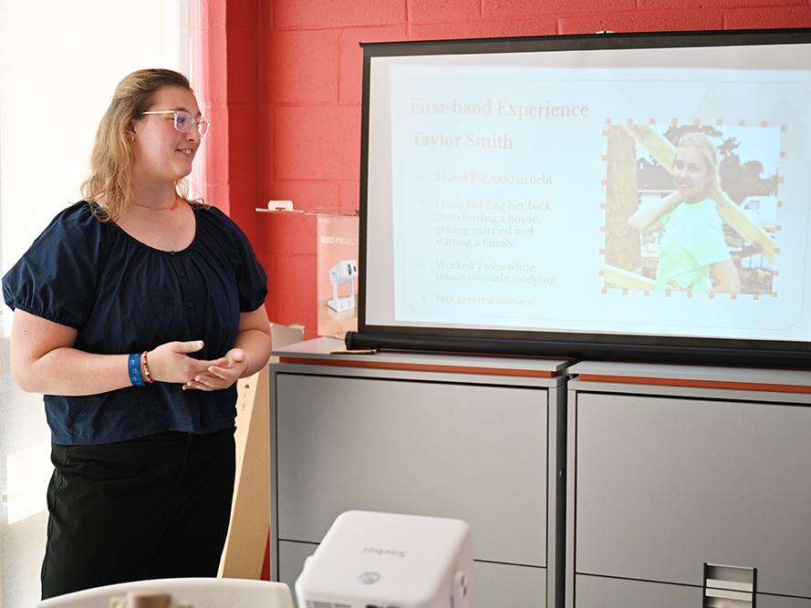 A high school student in a dark shirt gives a research presentation.