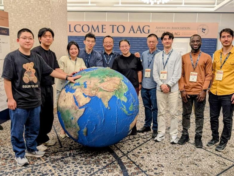 A group photo of Li and lab members smiling and posing together with a giant inflatable globe prop.
