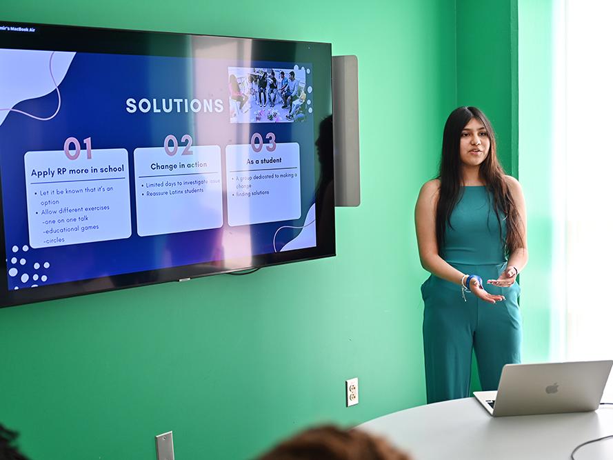 A high school student in a green outfit gives a research presentation.