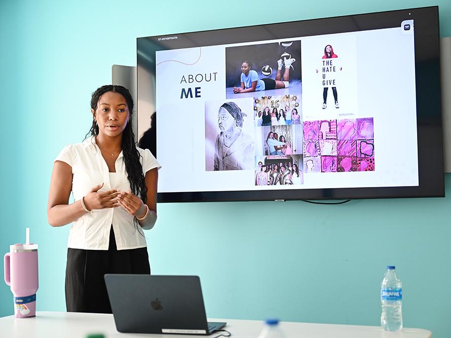 A high school student in a white shirt gives a research presentation.