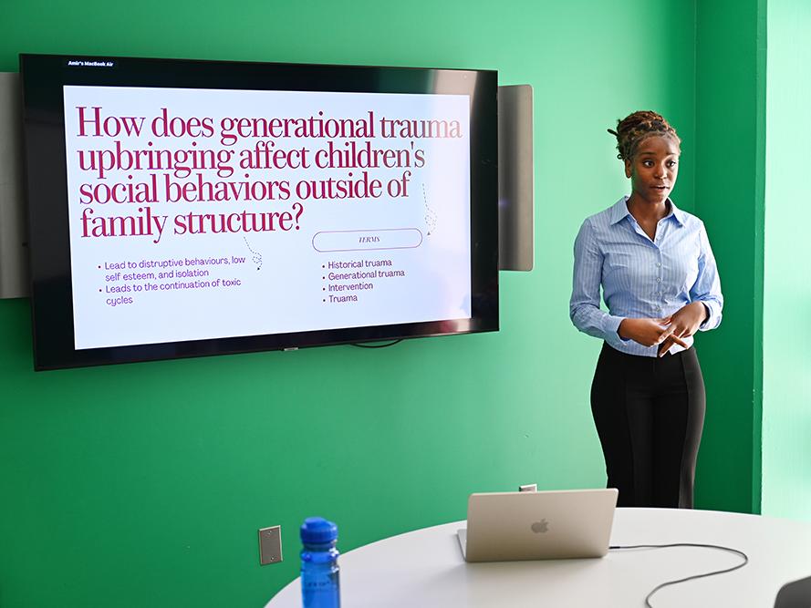 A high school student wearing a light color shirt gives a research presentation.