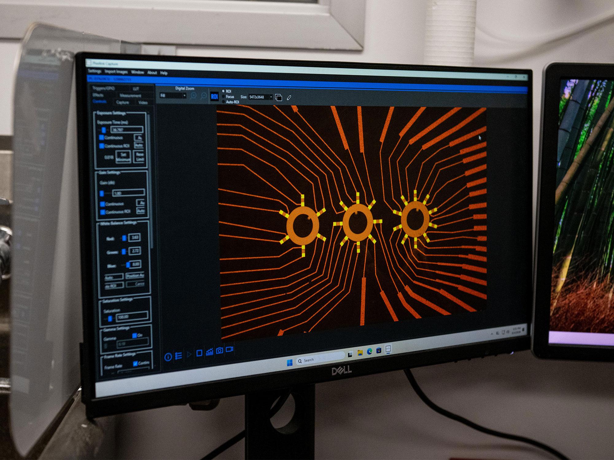 A computer monitor shows a blown up image of the team's devices taken from a microscope, showcasing the symmetrical contacts around the rings