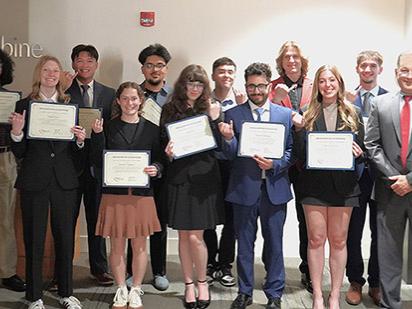 Engineering students pose for a group photo holding up their certificates and showing off their engineering rings by holding their pinky fingers in the air