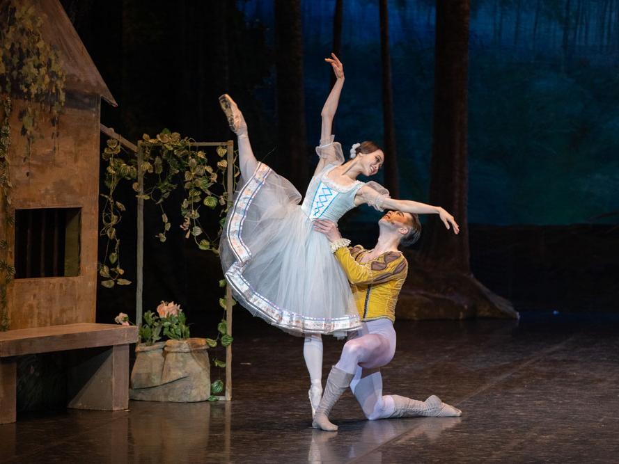A kneeling dancer holds a ballerina standing on one leg.