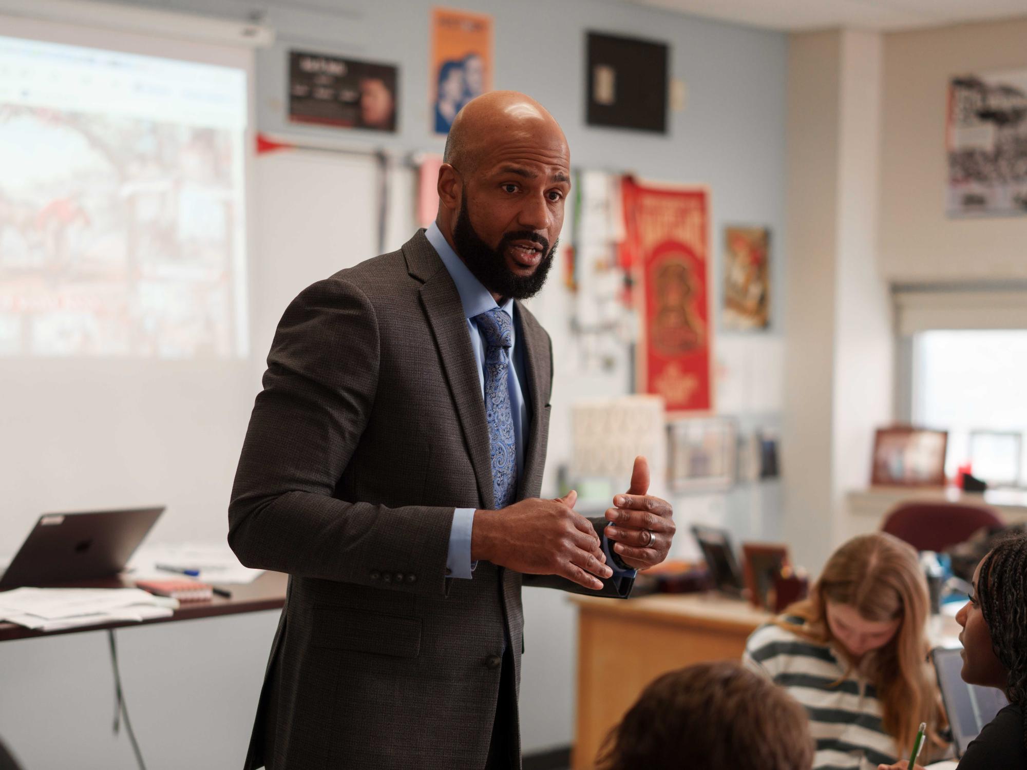 A man in a suit and tie speaks to students in a classroom.