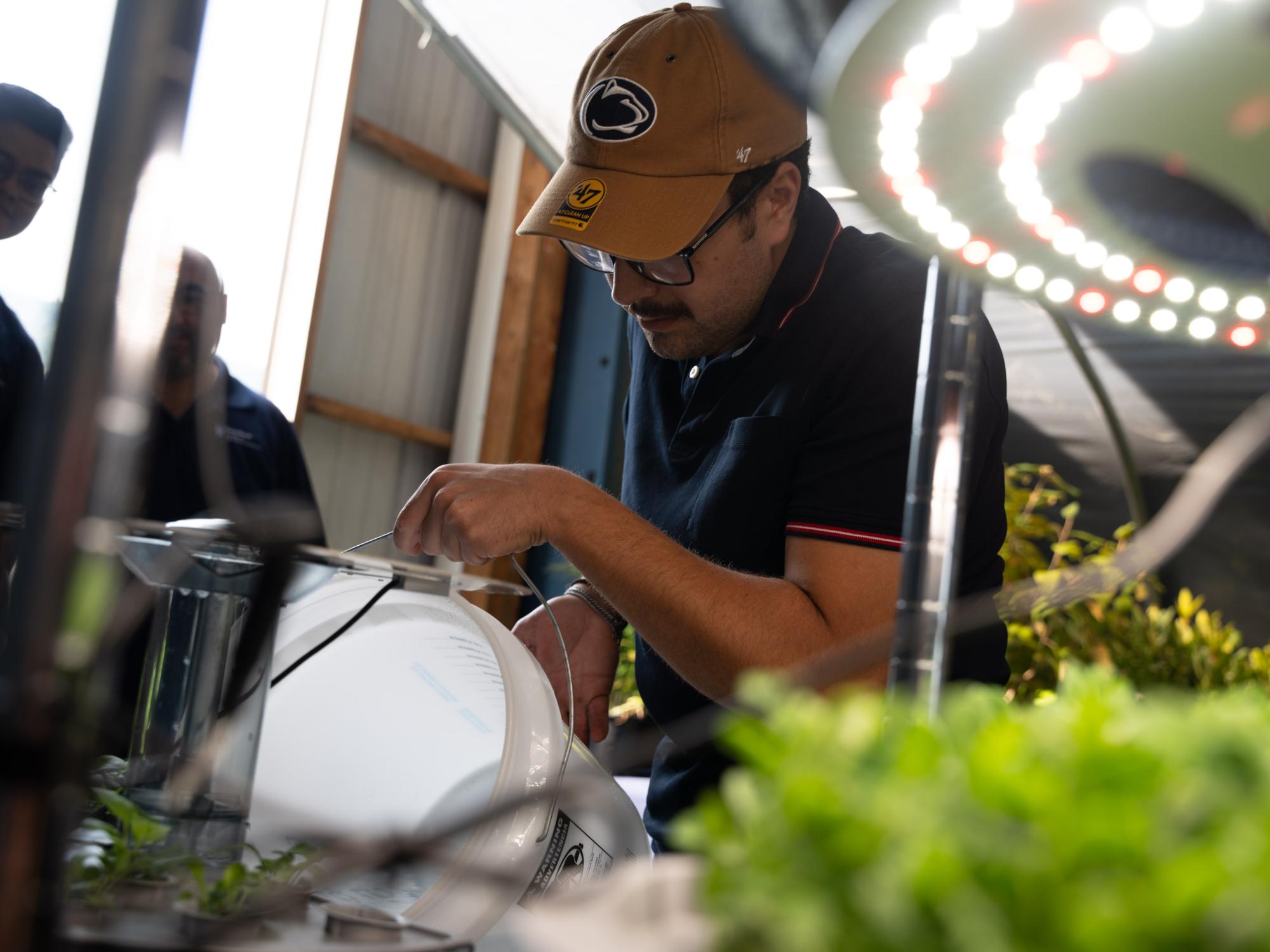 A person wearing a Penn State hat pours liquid from a white bucket
