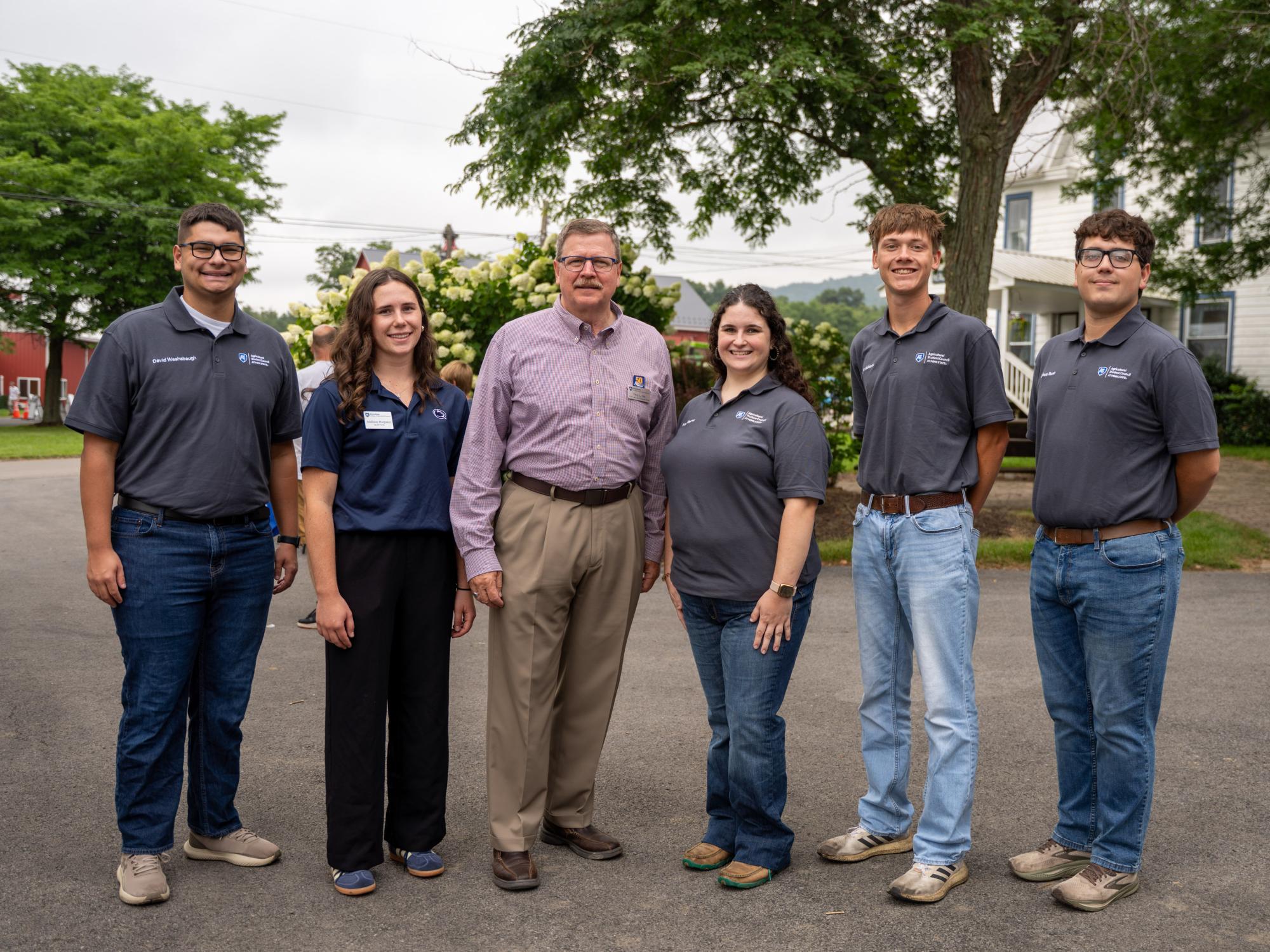 Six individuals stand outdoors and pose for the camera