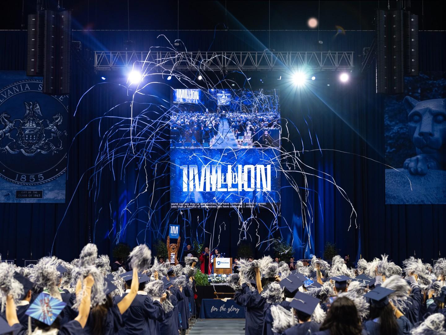 A wide shot of a commencement ceremony with streamers floating above graduates with a "1MILLION" sign in the center