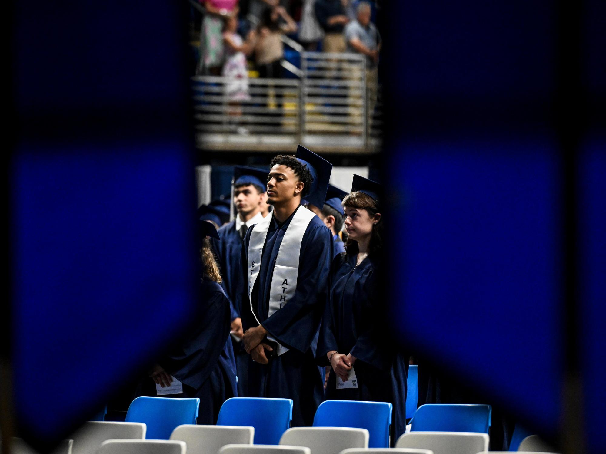 A focused picture of a graduate wearing a blue cap and gown while standing during a commencement ceremony