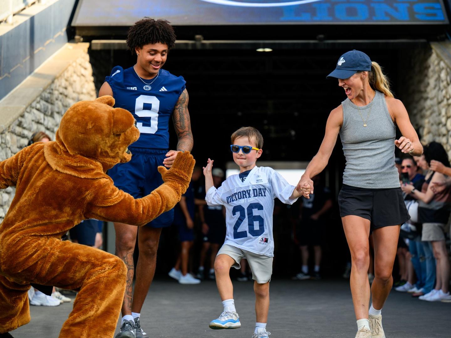 The Nittany Lion mascot high fives a child wearing a football jersey as he walks onto the field