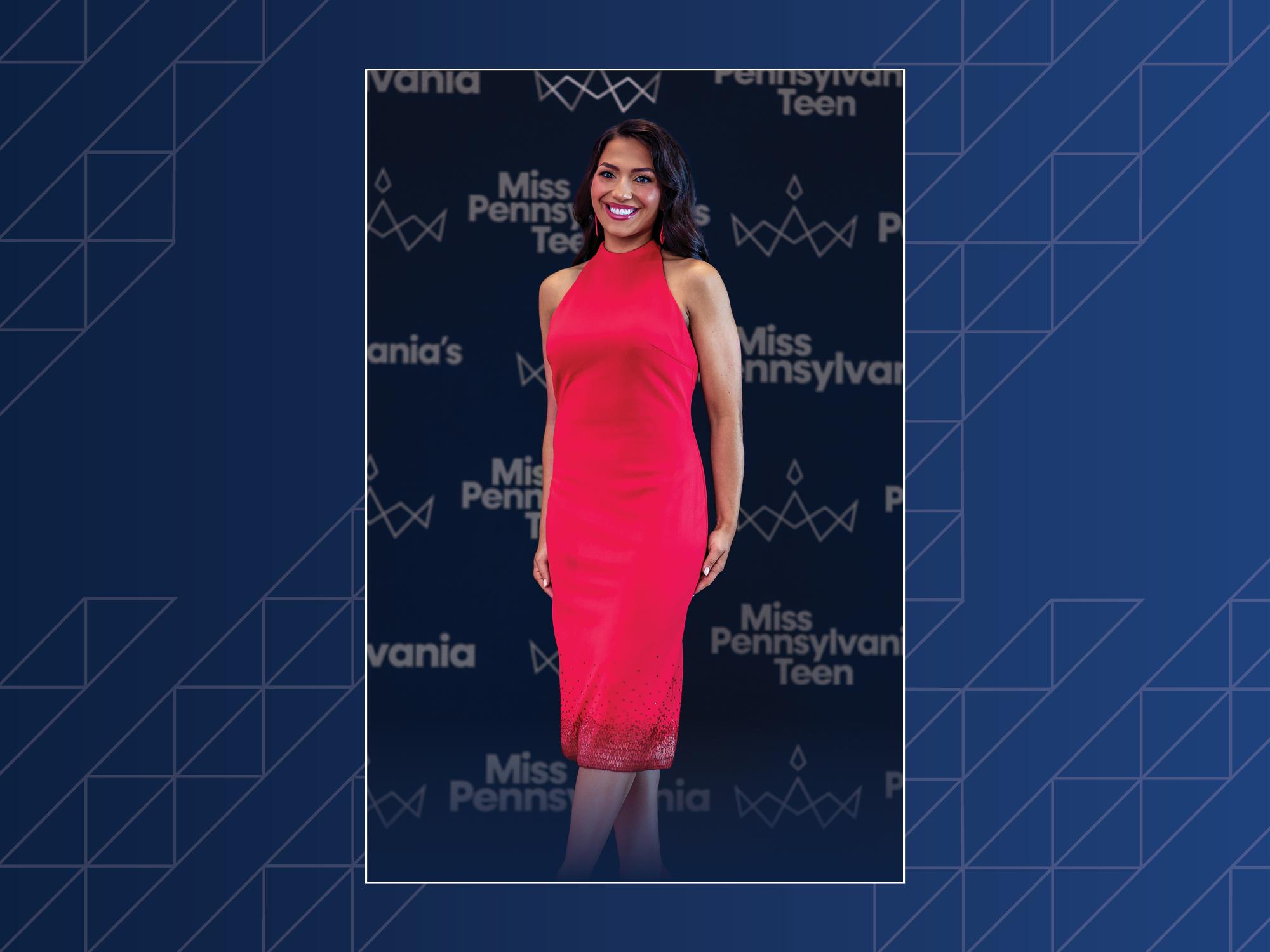 A woman wearing a red dress poses in front of a photo background that says, "Miss Pennsylvania 2026."