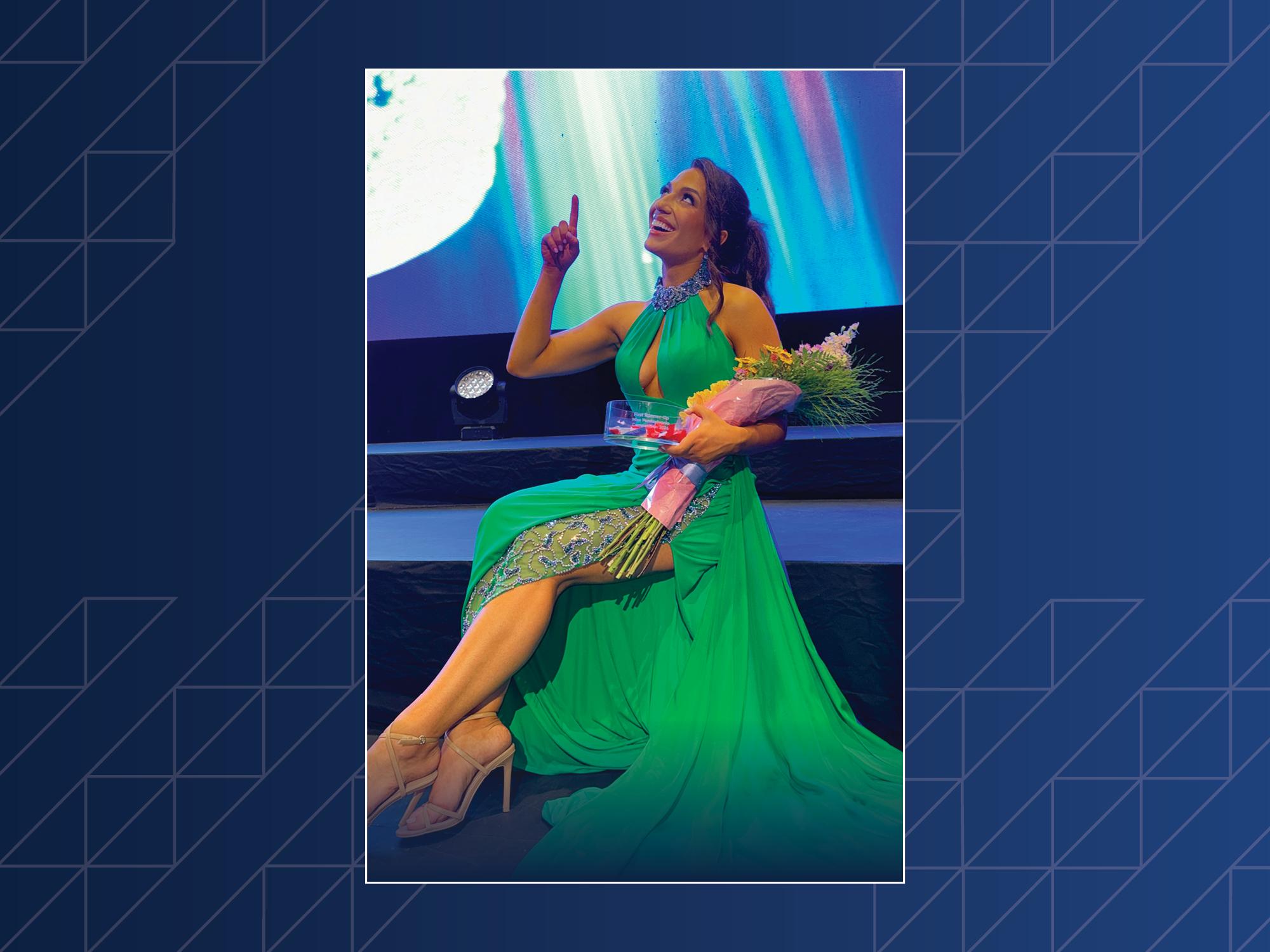 A woman wearing a green formal dress points on a stage.