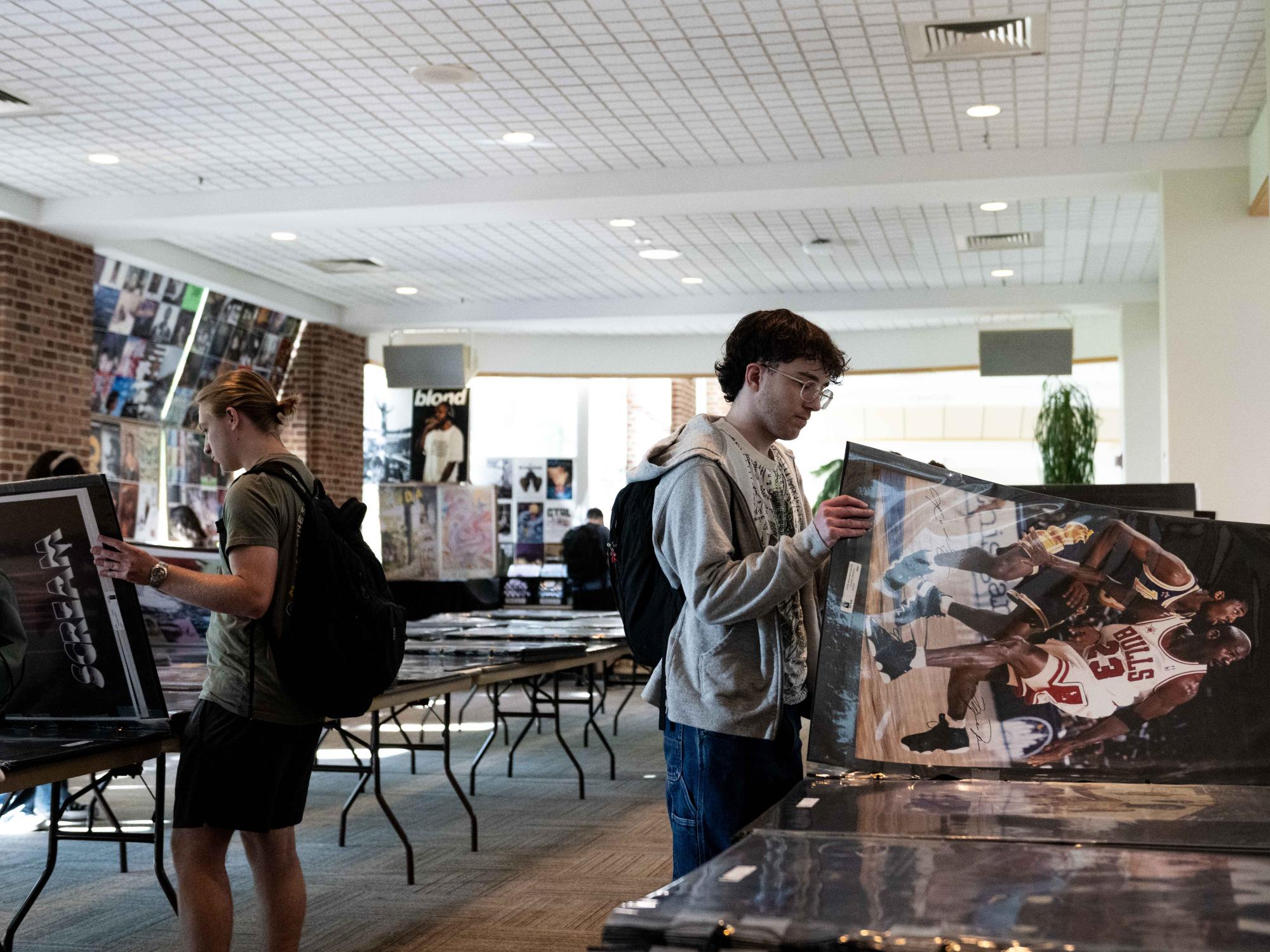 A student holds up a Michael Jordan basketball poster while browsing rows of posters and prints at a sale inside the HUB-Robeson Center.