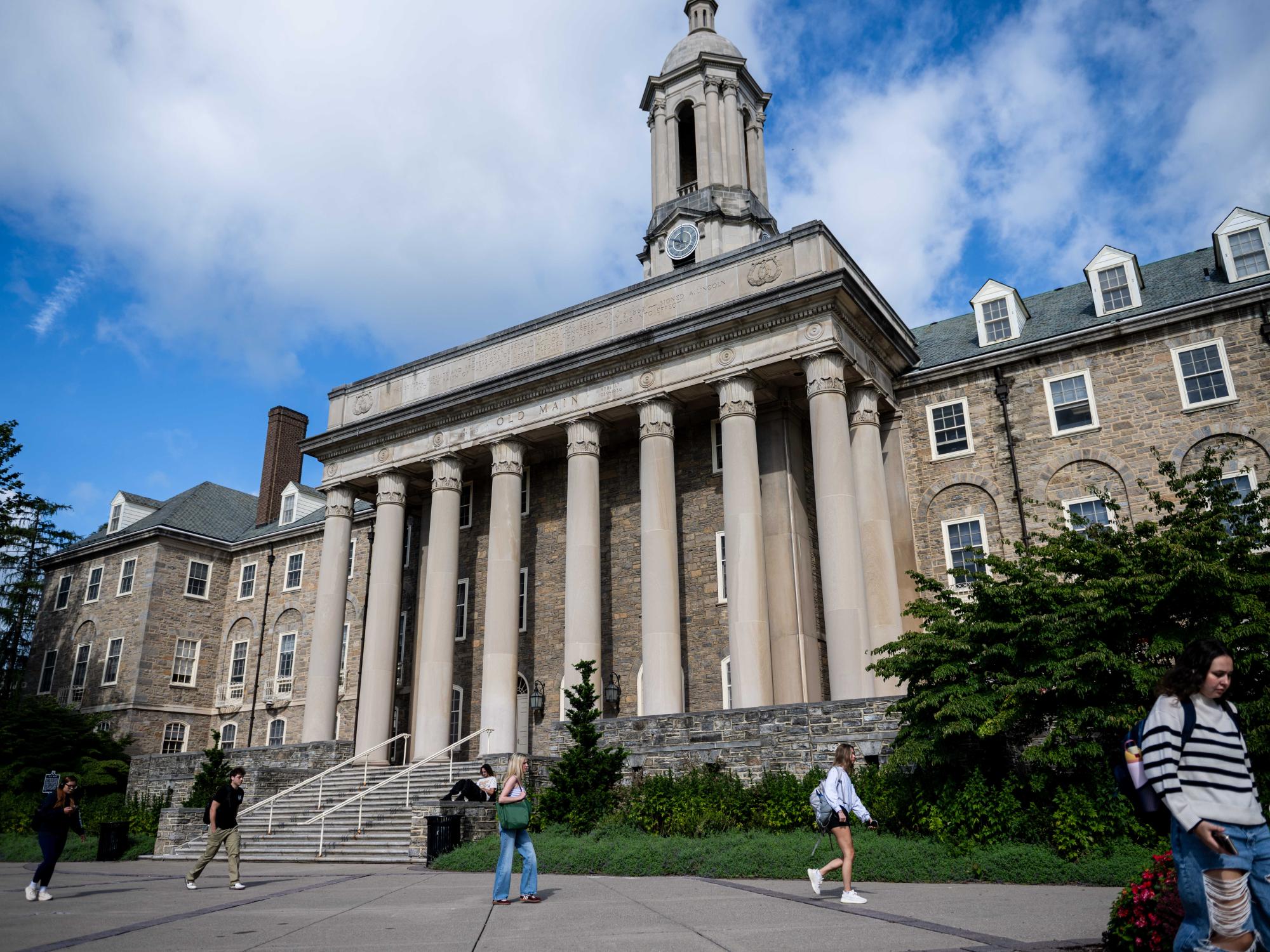 Students walk past Old Main under a bright blue sky