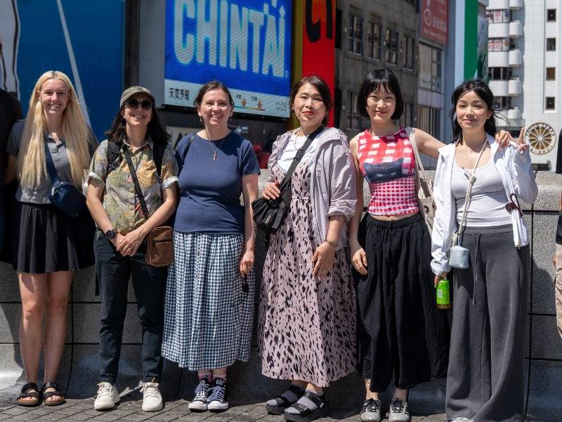 Penn State faculty and Asia Pacific Academic (APA) facilitators smile for a group photo in front of Osaka's iconic Glico Running Man sign in the vibrant Dotonbori entertainment district.