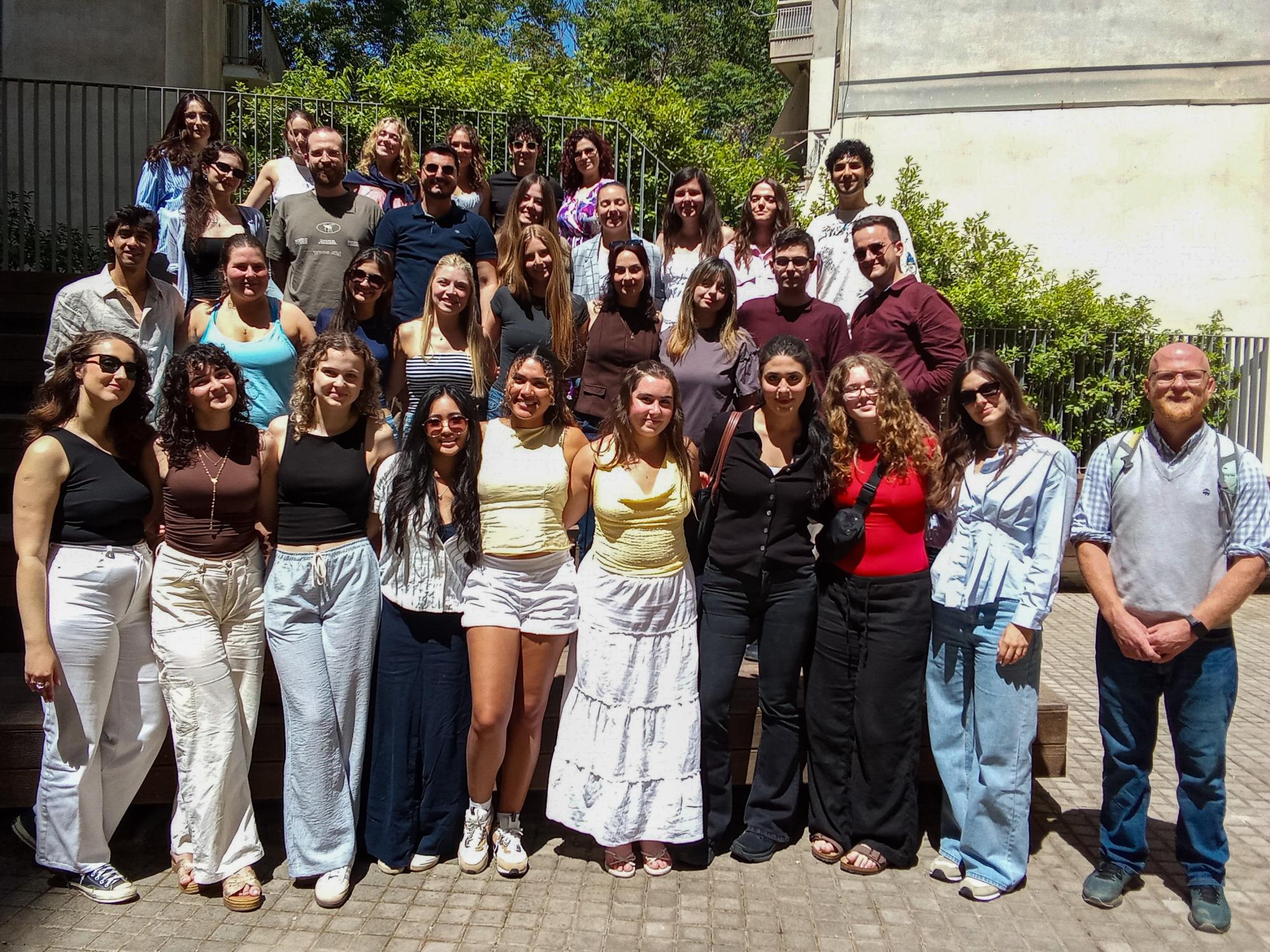 Karli Brenneman stands in a large group of students and faculty posed on outdoor steps, with trees and buildings in the background.