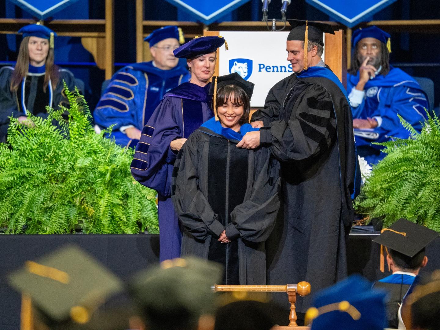 A graduating doctoral student is hooded by two advisers during a commencement ceremony