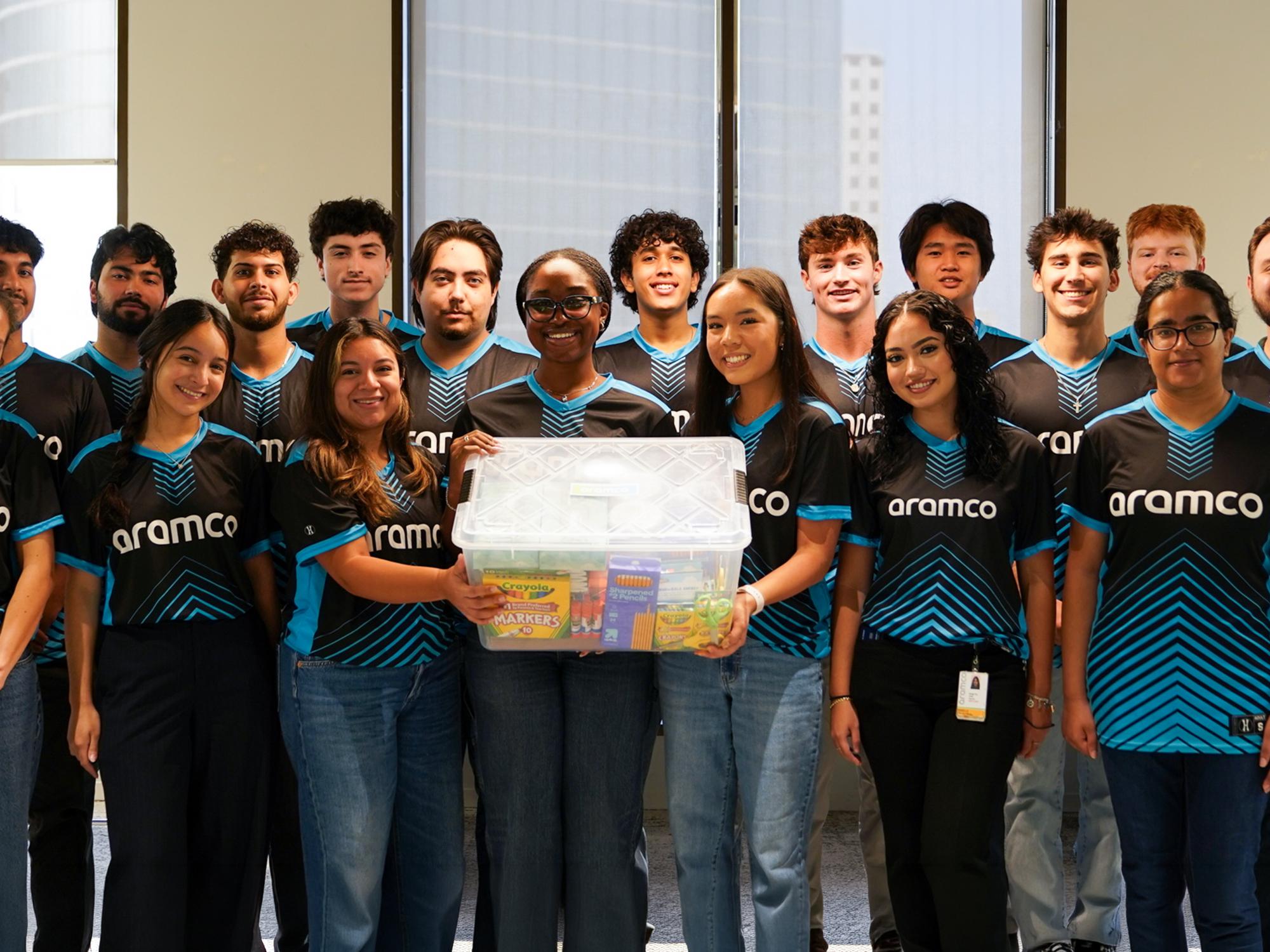 Osakiodeme Ikhinmwin holds a box of school supplies while surrounded by other interns all wearing shirts that read “Aramco.” 