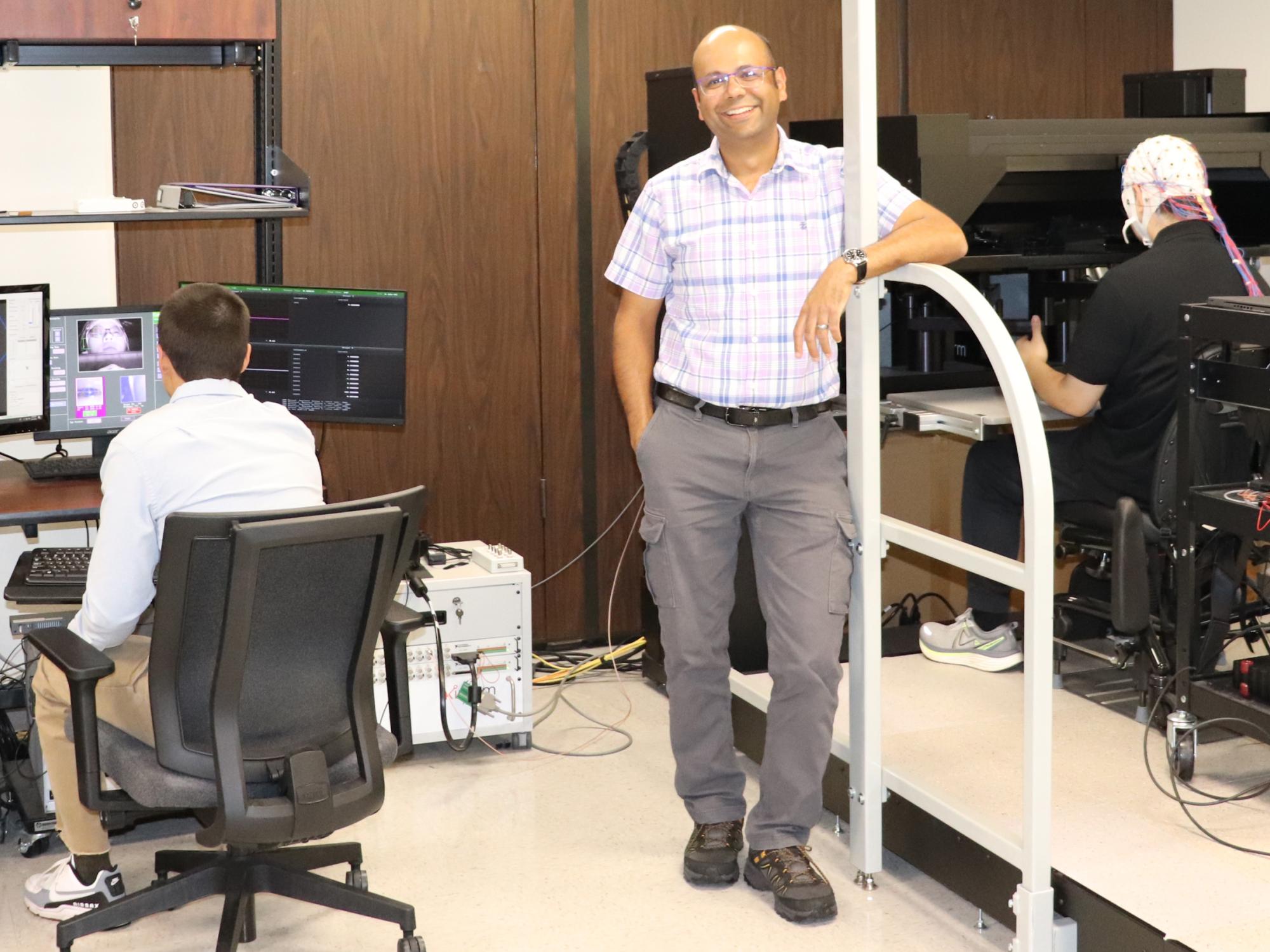 Tarkeshwar Singh standing in a lab setting, with seated lab member working at computers behind him