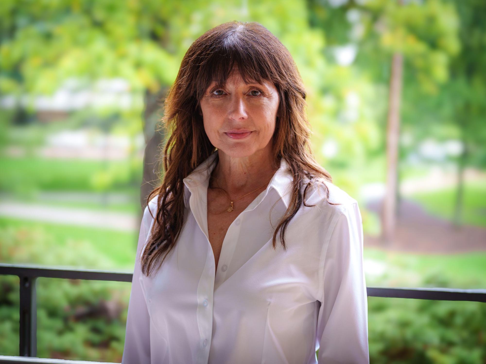 person with long dark hair and white blouse with greenery in background