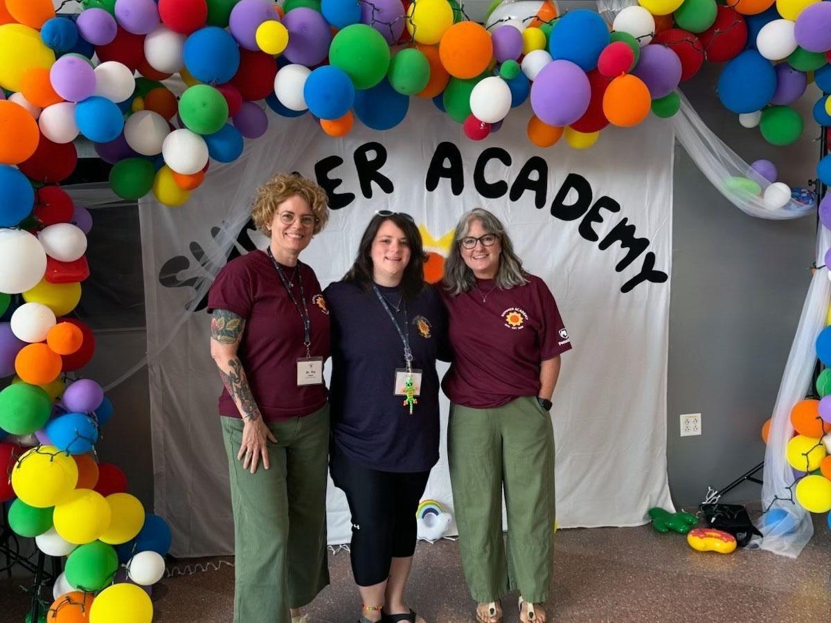 Pia Smal, Kiley Foley and Deirdre O’Sullivan stand together beneath a colorful balloon display at the Penn State Summer Academy.