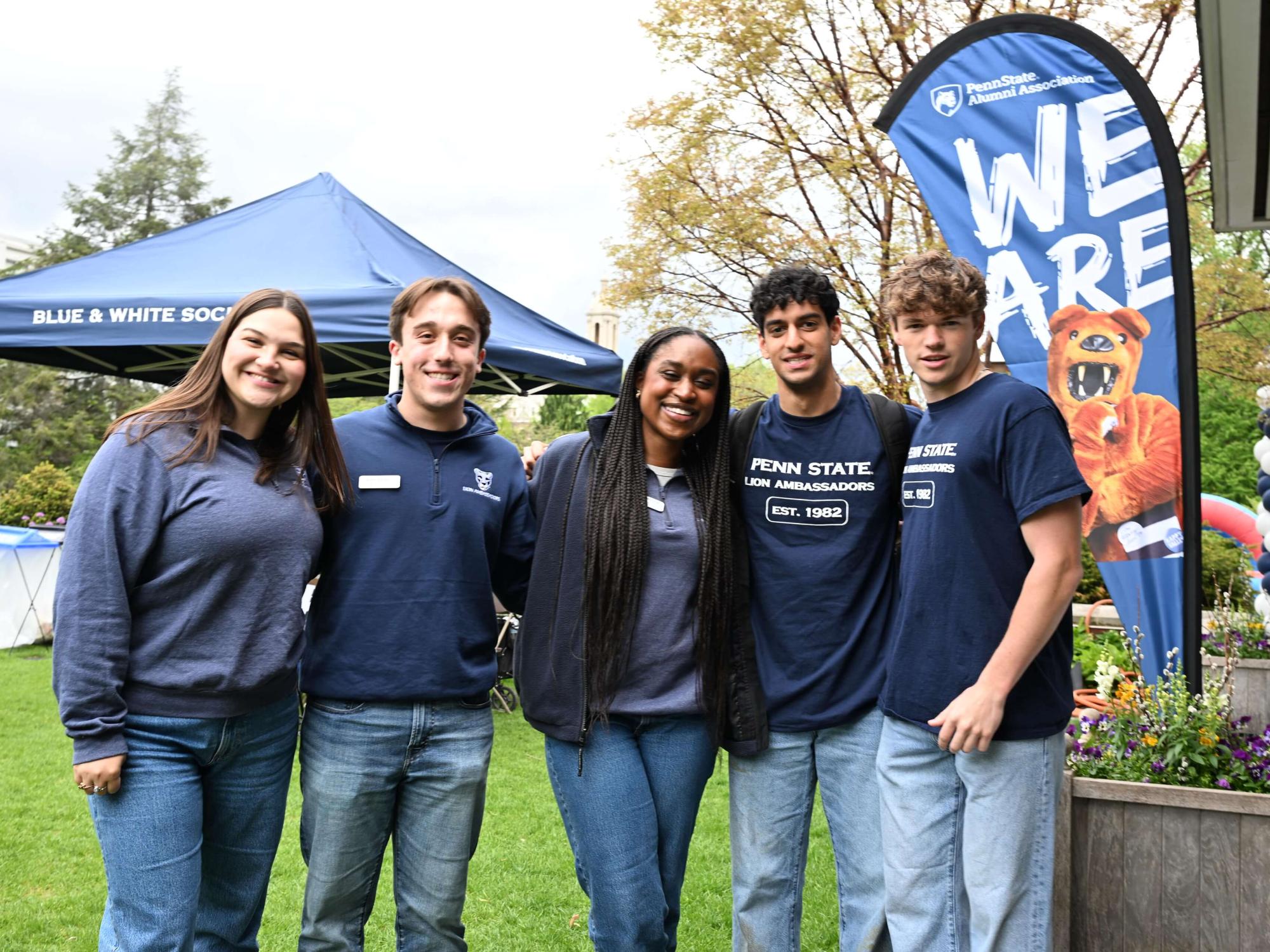 Osakiodeme Ikhinmwin (right) stands with two other Lion Ambassadors in front of a blue and white balloon arch in front of the steps of Old Main.