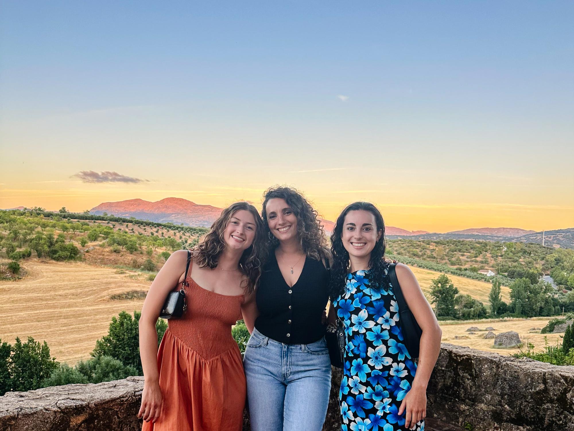 Three people pose for a photo in a picturesque outdoor setting with a beautiful sunset.