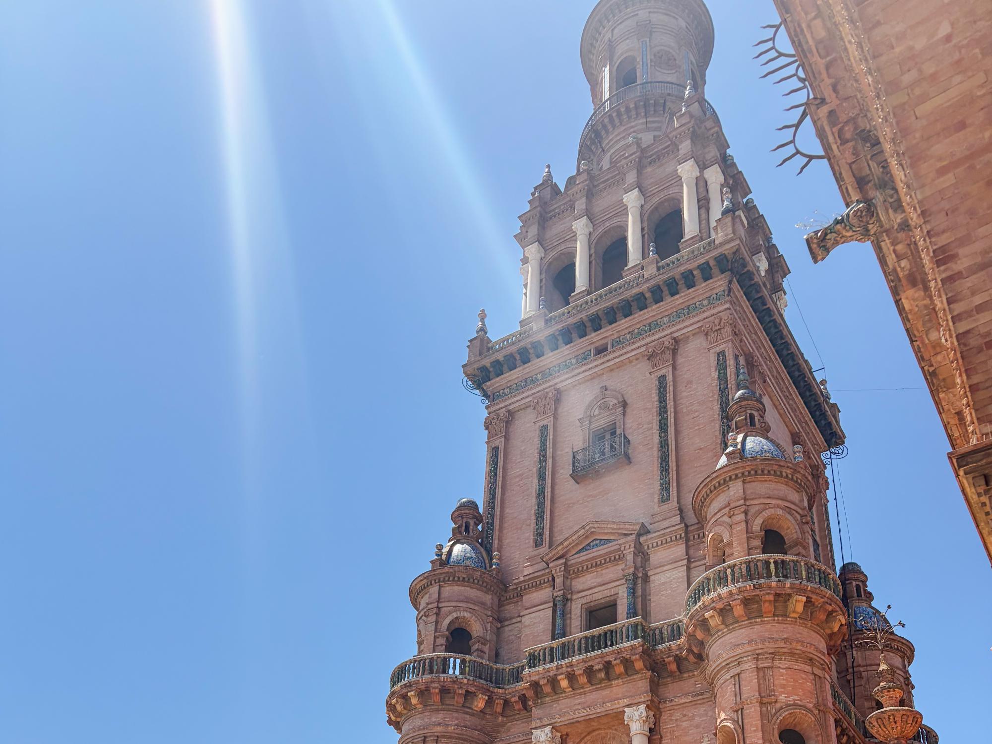 A tall, ornate tower is illuminated by a bright, clear sky and a shining sun.