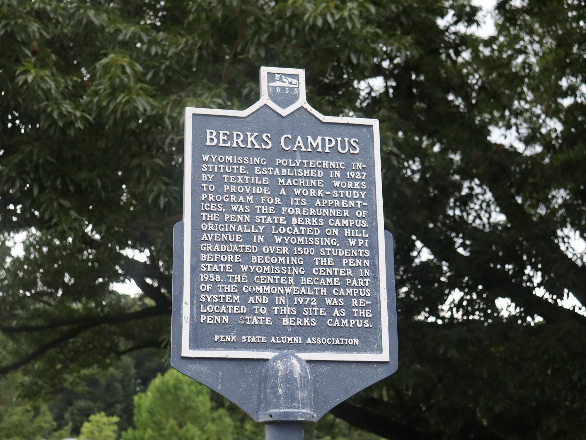 A blue historical marker sign in front of trees.