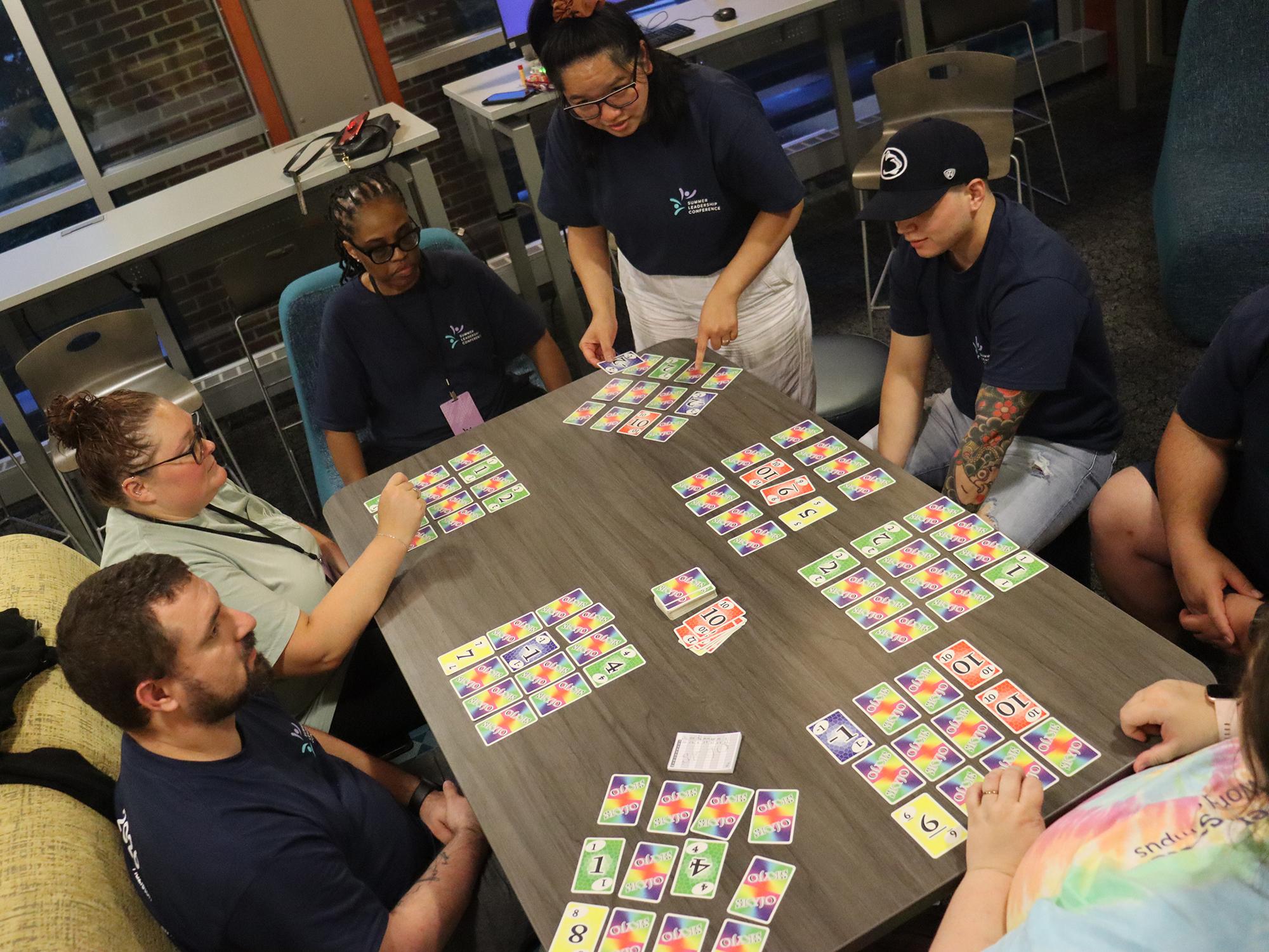 A group of people playing a card game around a table.