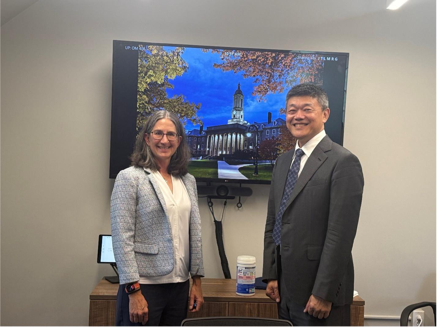 Two individuals smile for a picture in front of an image of Old Main