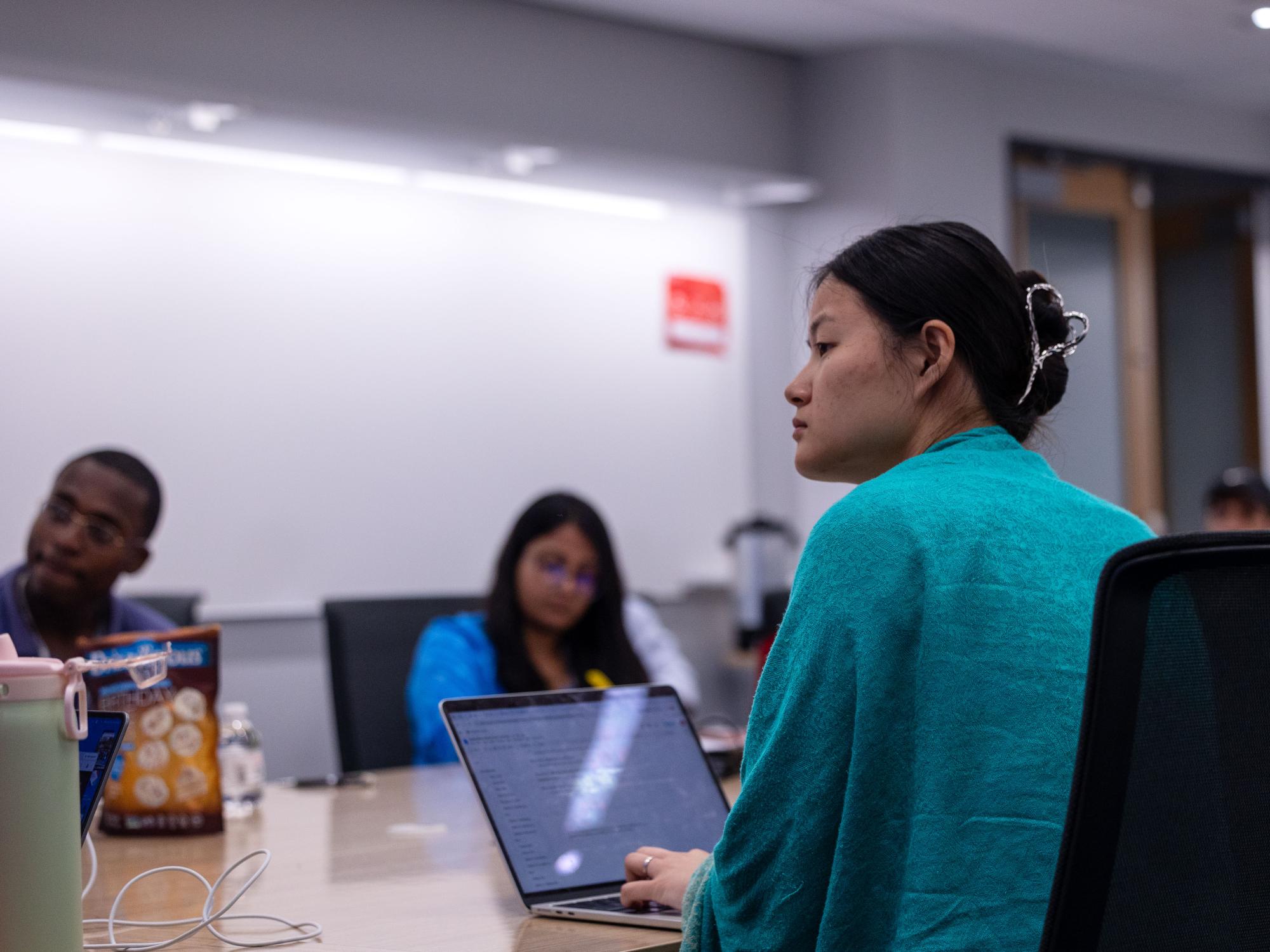 Celine Tsoi wears a teal sweater and listens intently to a presenter. 
