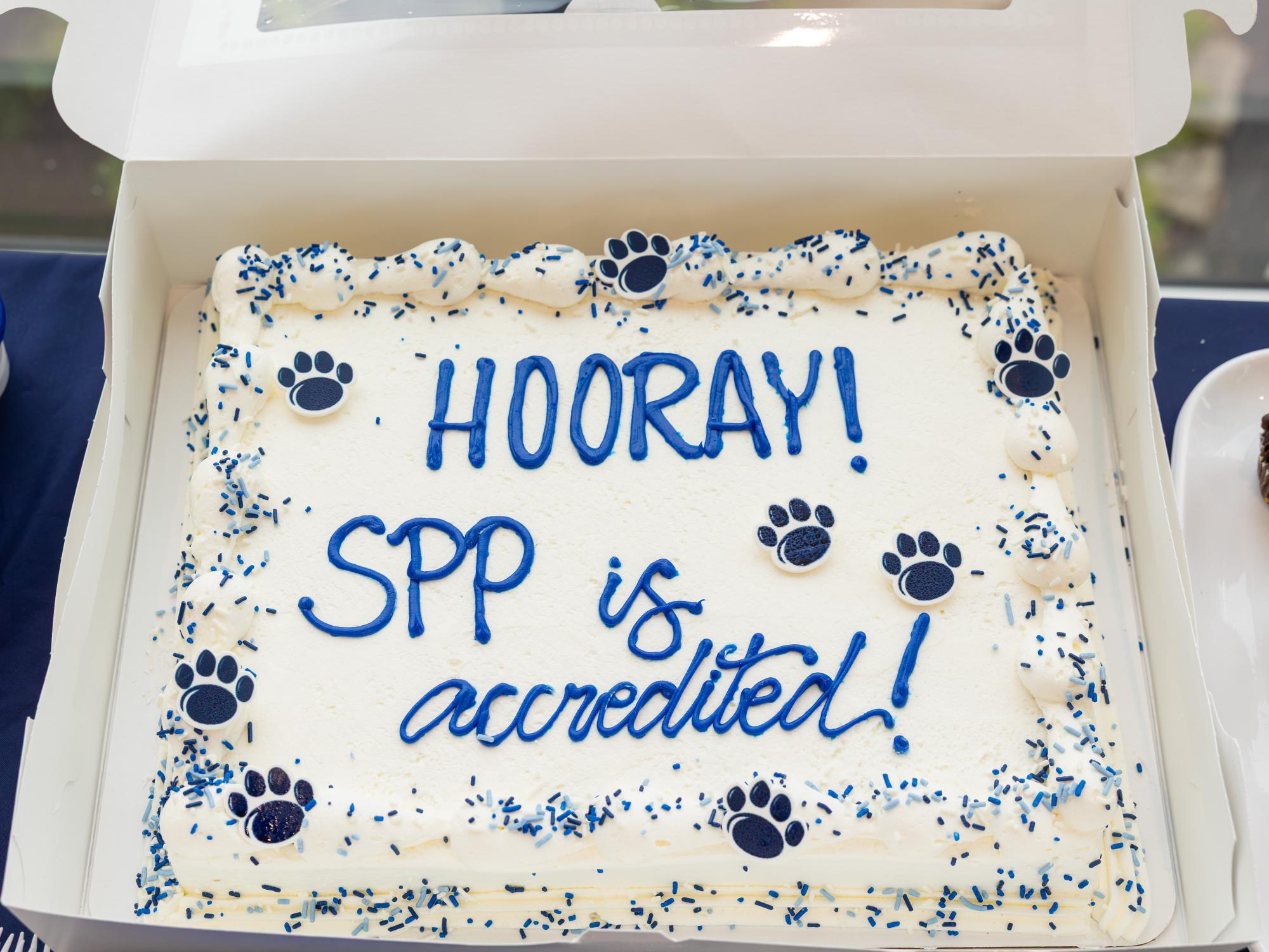 A cake with white icing and blue lettering celebrating the School of Public Policy's accreditation. 