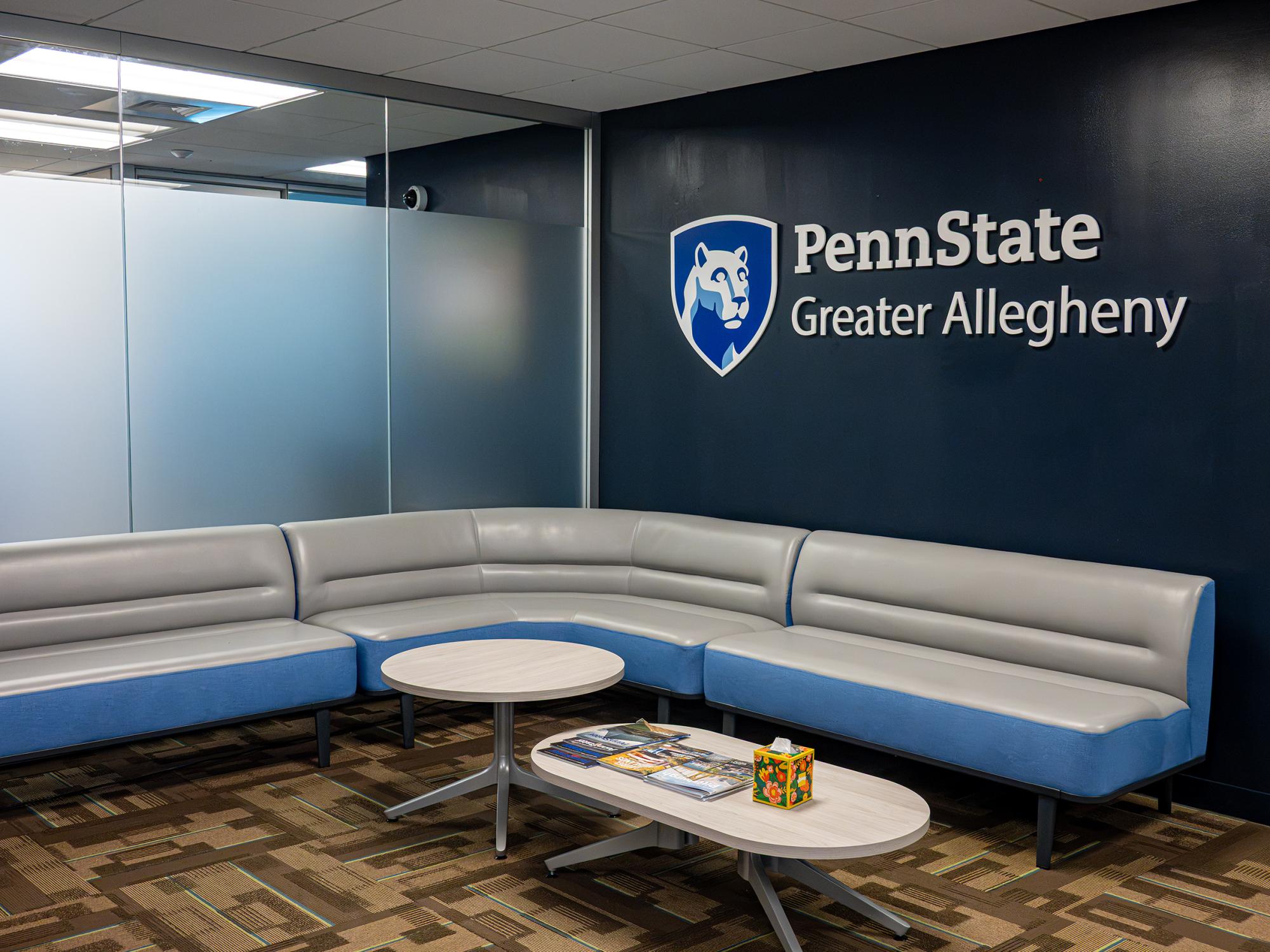 A lounge area in the Admissions and Student Aid suite includes comfortable seating and a Penn State Greater Allegheny wall sign displayed against a blue accent wall.