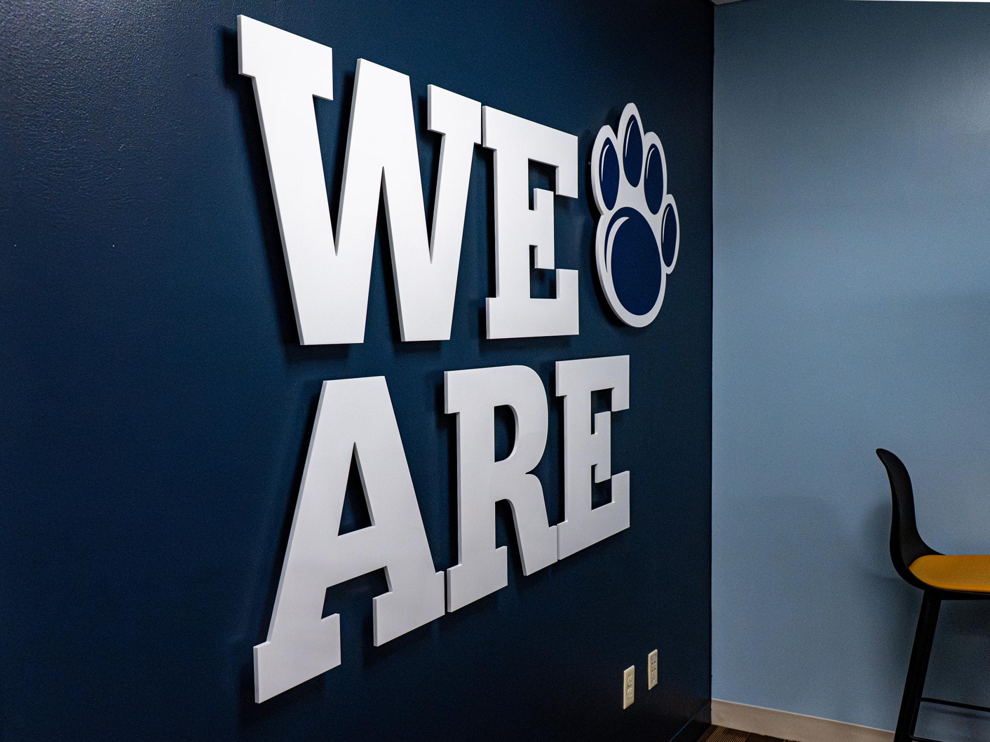 Large white letters spelling “WE ARE” and a Penn State paw graphic are mounted on a blue accent wall inside the Admissions and Student Aid suite.
