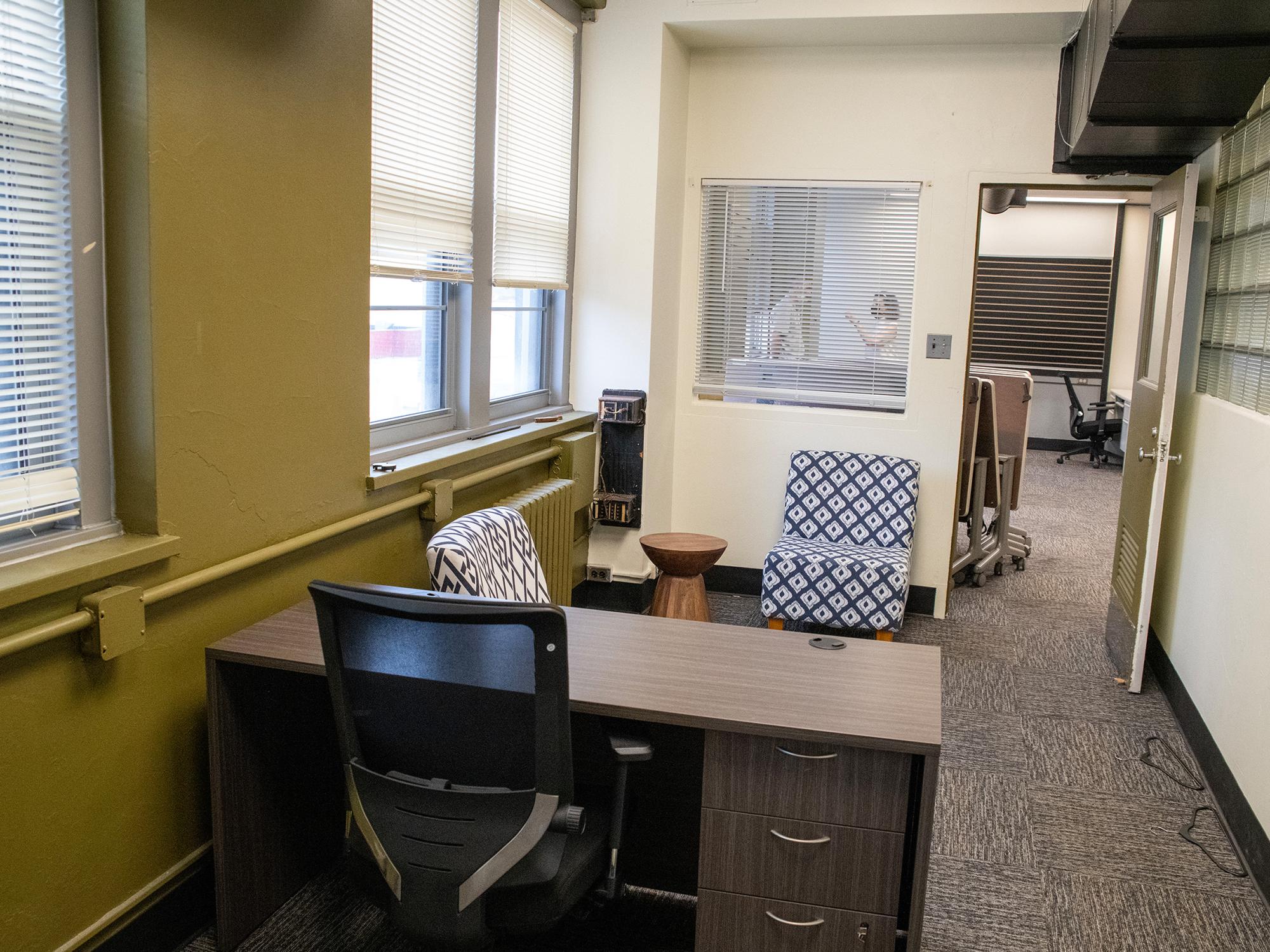 A furnished office at the Mon Valley LaunchBox includes a desk, seating area, and natural light from large windows overlooking the downtown area.