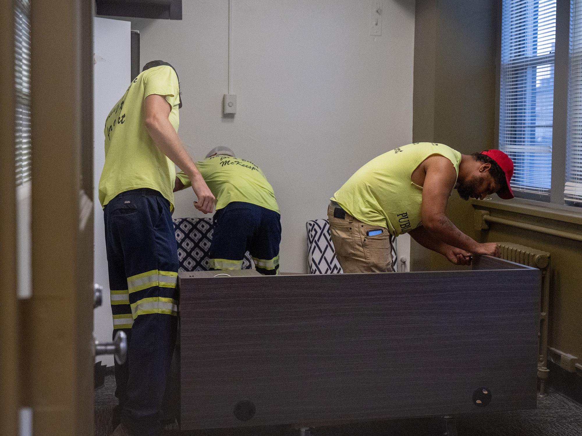 Several City of McKeesport workers assemble office furniture inside a workspace at the new Mon Valley LaunchBox location, helping prepare the facility for opening.