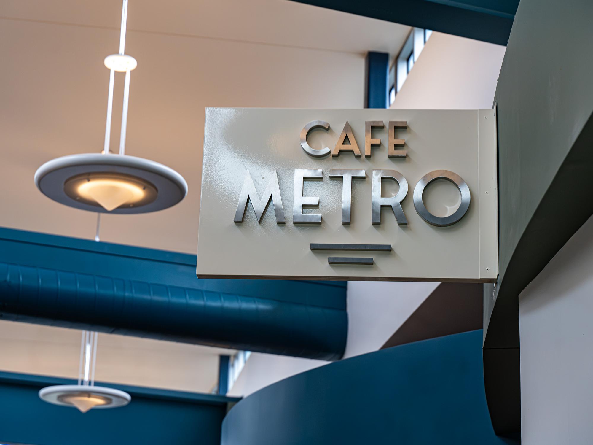 A modern “Café Metro” sign hangs above the dining area in the Student Community Center, with blue architectural accents and pendant lighting visible in the background.
