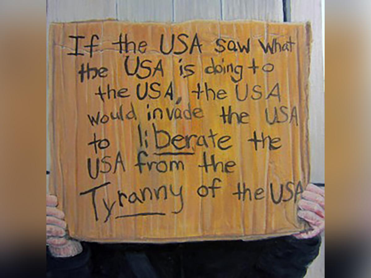 Handwritten cardboard sign reads: If the USA saw what the USA is doing to the USA, the USA would invade the USA.