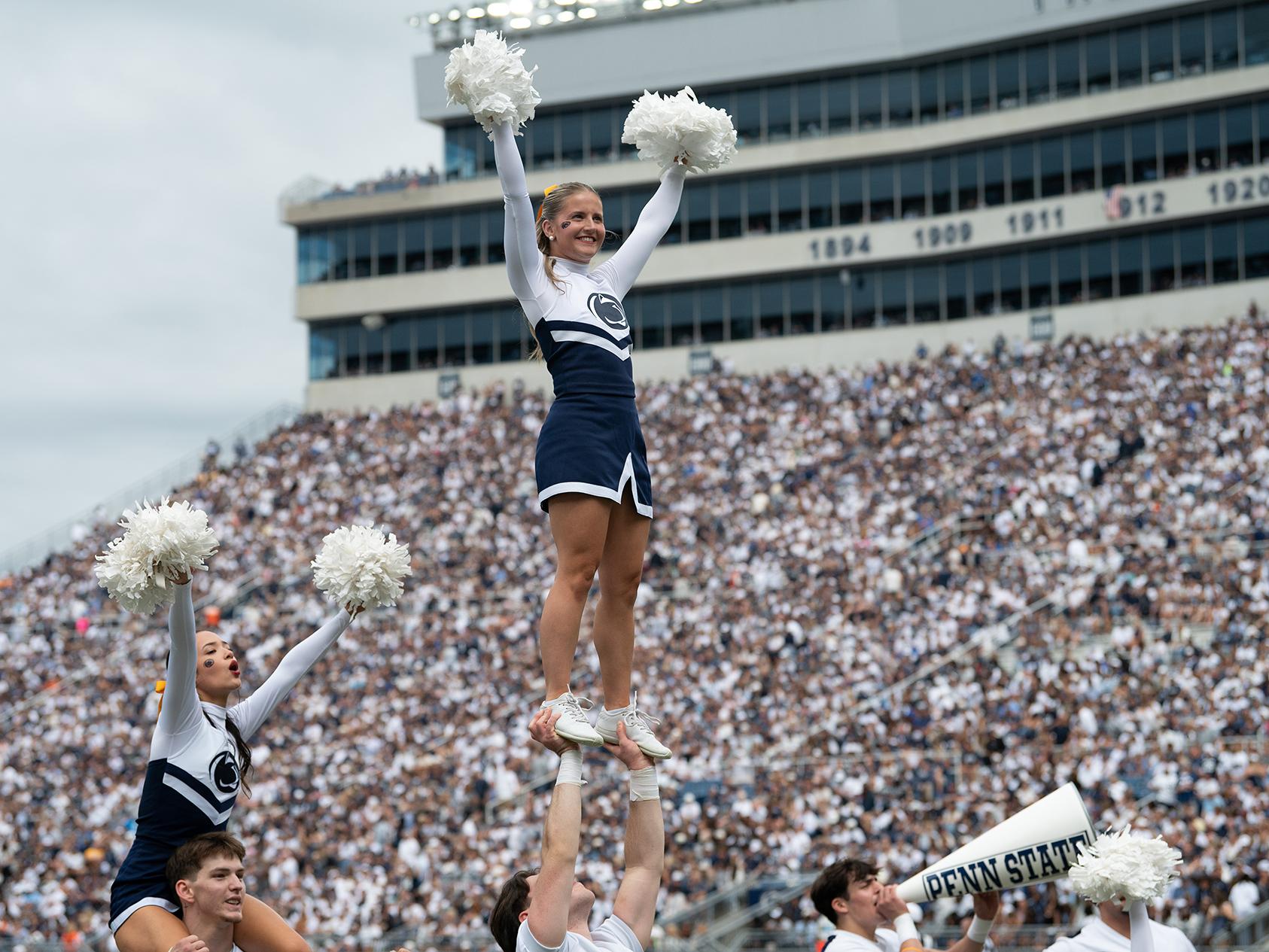Male cheerleader holds up female cheerleader