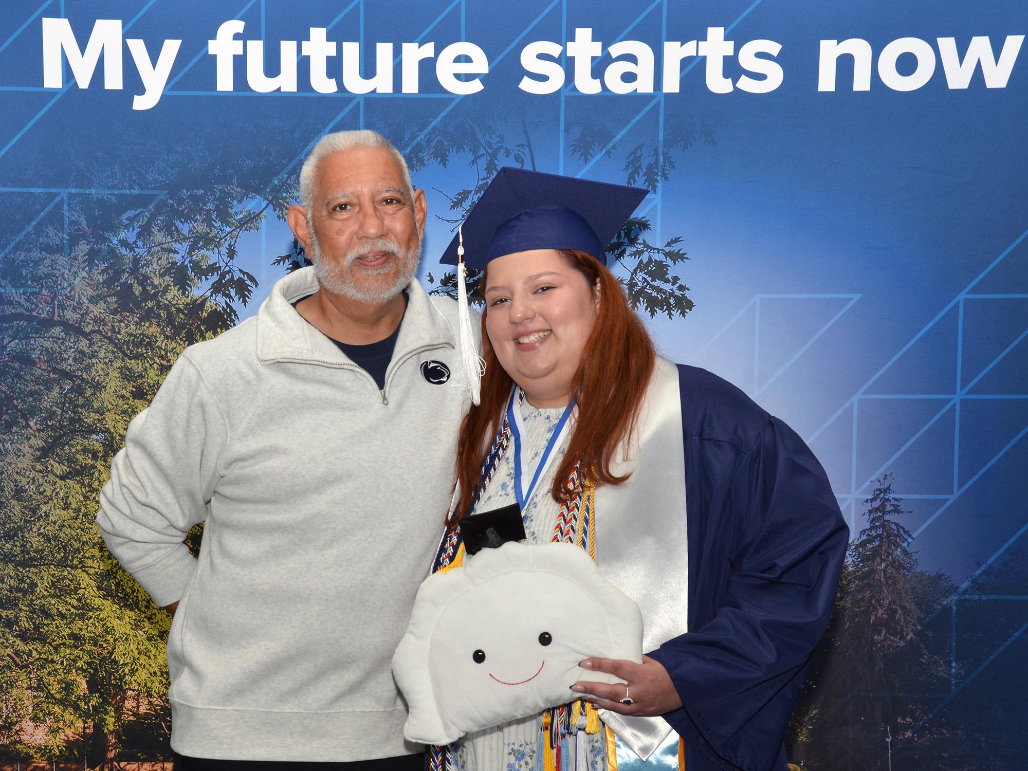 A man and a woman pose in front of a Penn State photo background.