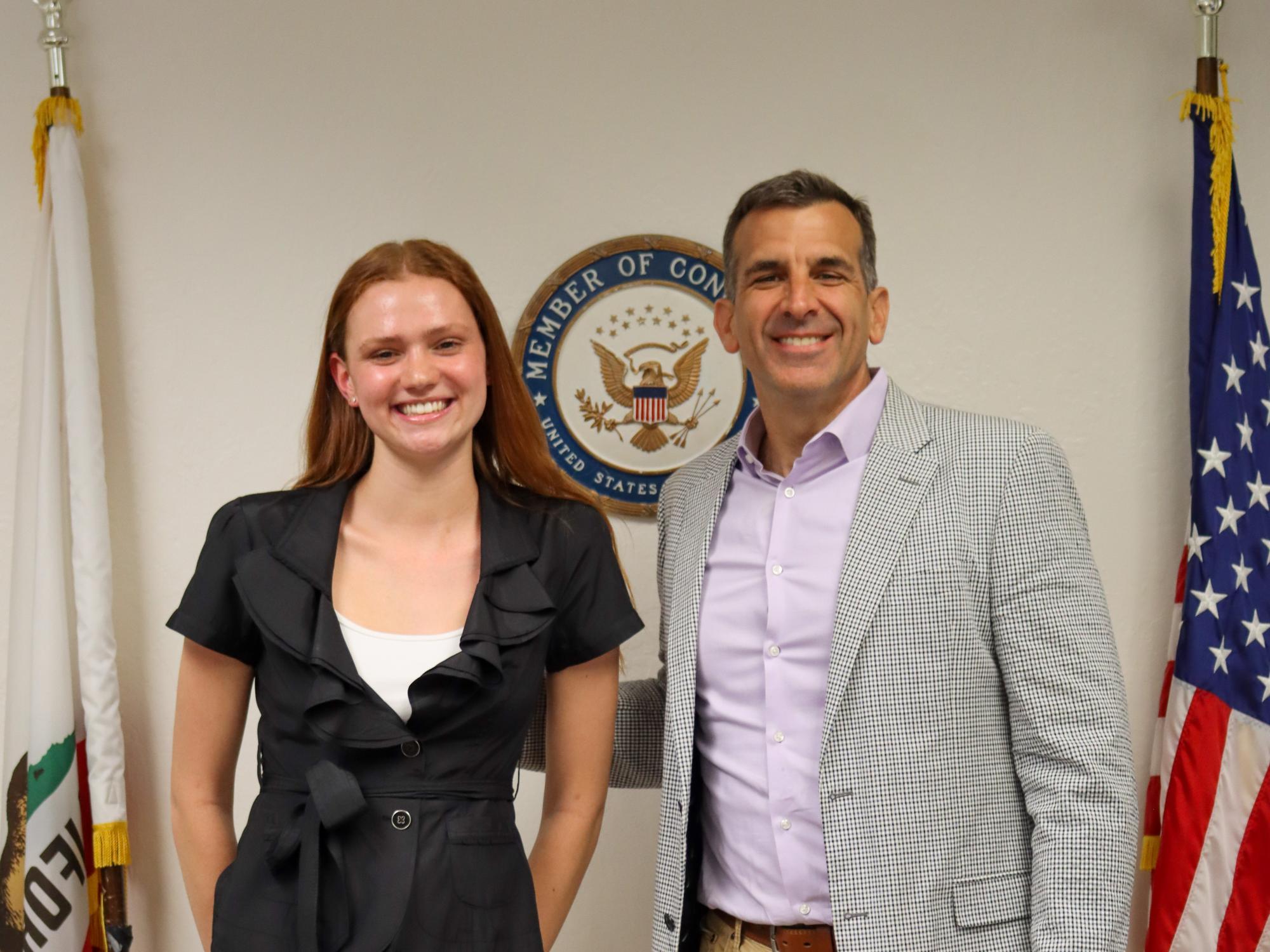 Odessa Dando (left) in a suit and Congressman Liccardo (right) in casual attire standing in front of the United States flag and the state seal.