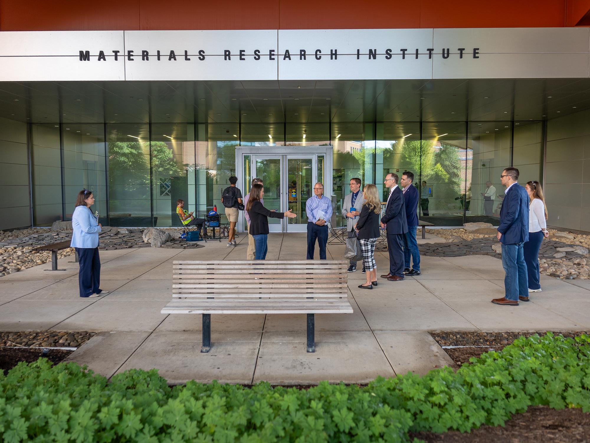 A group of professionals stand outside of a large research facility