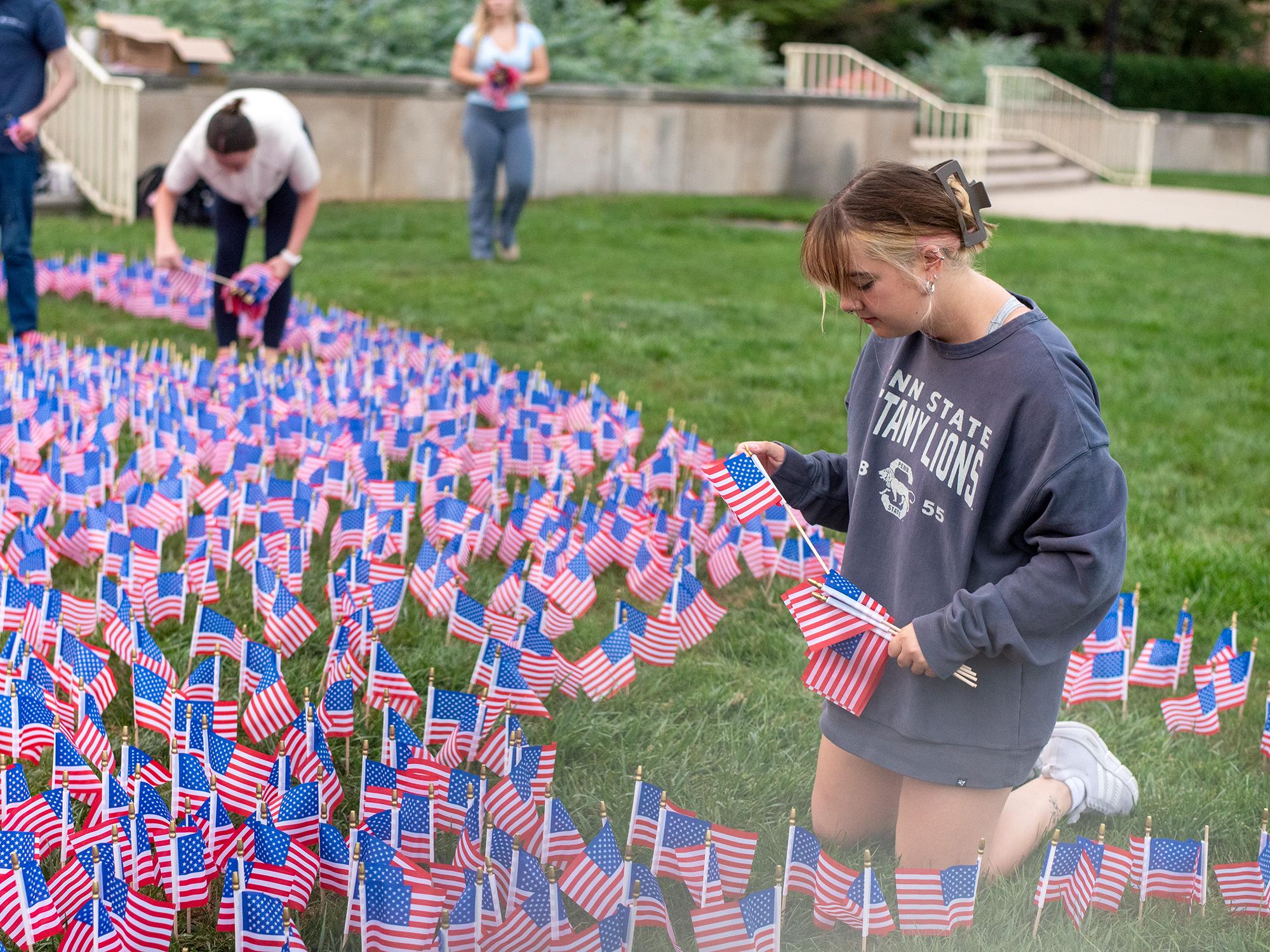 A student plants mini American flags in the grass with others around them doing the same