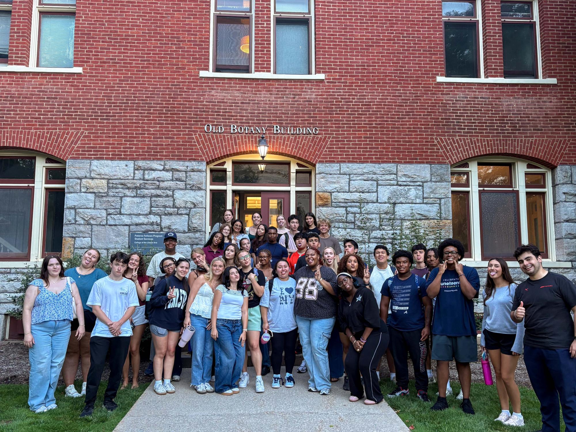 A group of approximately 40 students stands together outside the entrance to Old Botany Building.