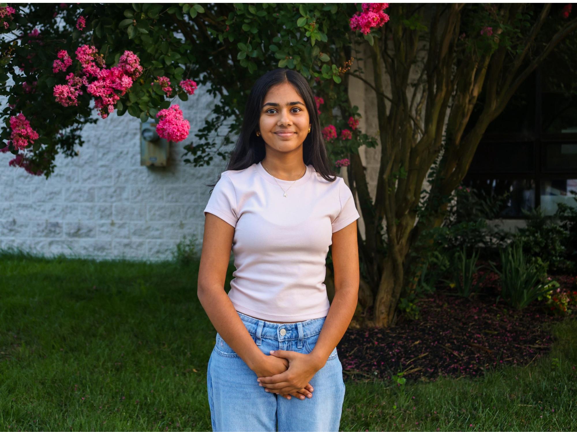 person with long dark hair wearing pink shirt and jeans